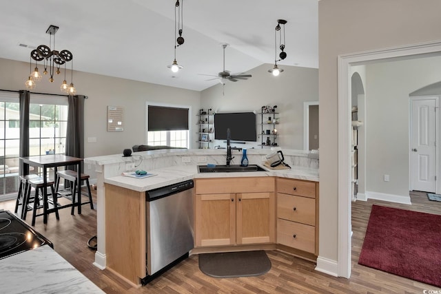 kitchen featuring light brown cabinetry, stainless steel dishwasher, vaulted ceiling, and hardwood / wood-style flooring