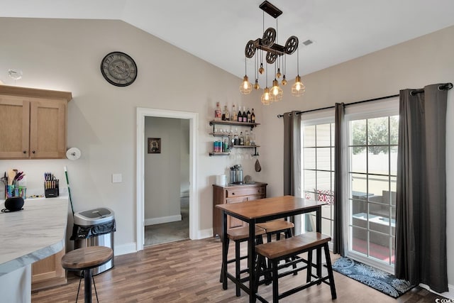 dining space with indoor bar, light hardwood / wood-style floors, and vaulted ceiling