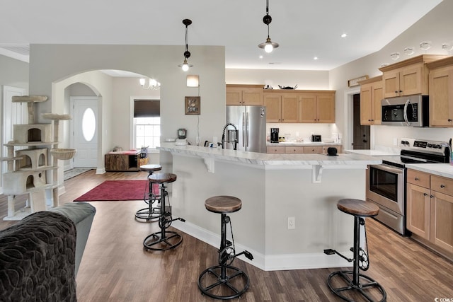 kitchen with pendant lighting, a center island with sink, hardwood / wood-style flooring, a kitchen bar, and stainless steel appliances