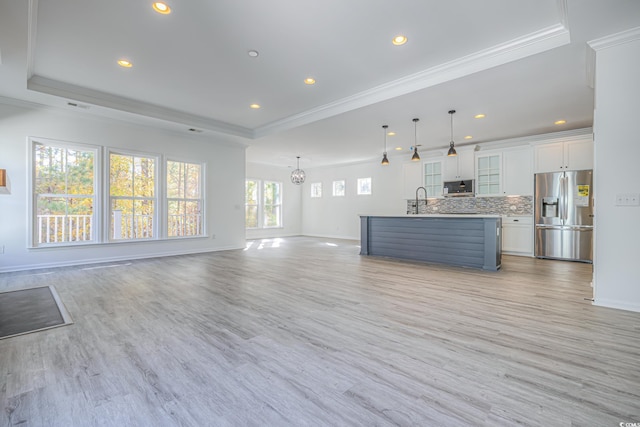 unfurnished living room featuring a tray ceiling, crown molding, sink, a notable chandelier, and light hardwood / wood-style floors