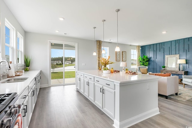 kitchen with light wood-type flooring, white cabinetry, hanging light fixtures, and sink