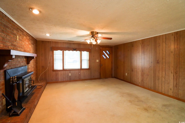 carpeted living room featuring a wood stove, ceiling fan, wood walls, crown molding, and a textured ceiling