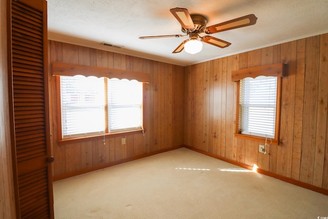 carpeted spare room with ceiling fan, wooden walls, and ornamental molding