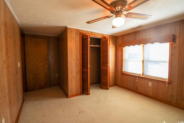 unfurnished bedroom with ceiling fan, light colored carpet, a textured ceiling, wooden walls, and a closet