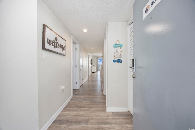 hallway with a textured ceiling and light hardwood / wood-style flooring