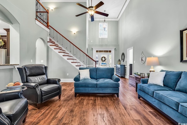 living room with a towering ceiling, dark hardwood / wood-style floors, ceiling fan, and crown molding