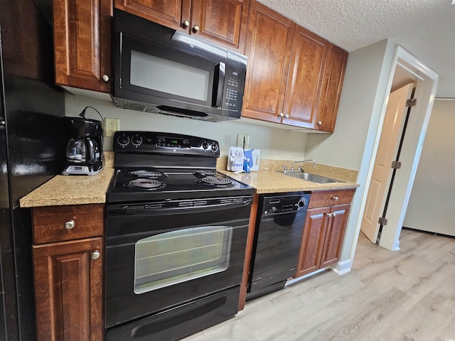 kitchen with sink, light hardwood / wood-style flooring, black appliances, and a textured ceiling