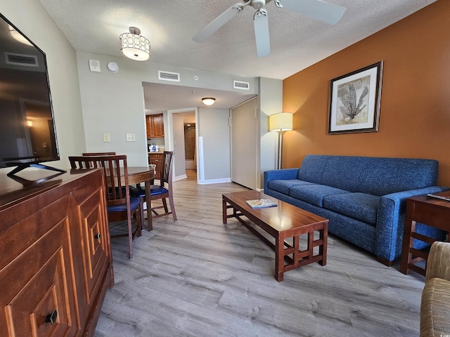 living room featuring ceiling fan, light hardwood / wood-style flooring, and a textured ceiling