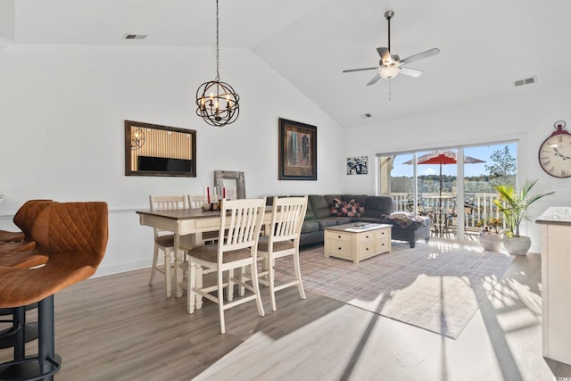 dining room featuring hardwood / wood-style floors, ceiling fan with notable chandelier, and high vaulted ceiling