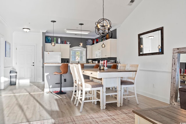 dining area with light wood-type flooring, an inviting chandelier, and ornamental molding