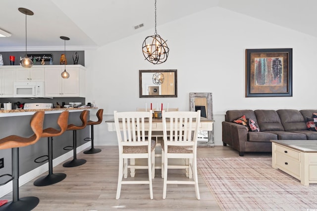 dining room featuring light hardwood / wood-style flooring, ornamental molding, lofted ceiling, and a notable chandelier