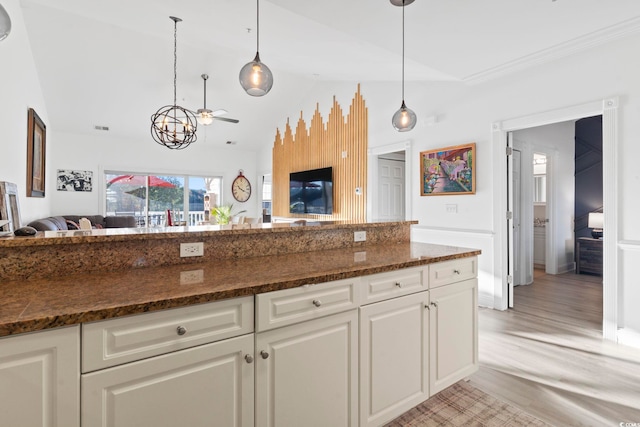 kitchen featuring pendant lighting, lofted ceiling, dark stone counters, and light hardwood / wood-style flooring