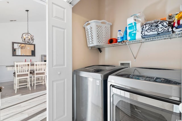 laundry room with a chandelier, light wood-type flooring, and washing machine and clothes dryer