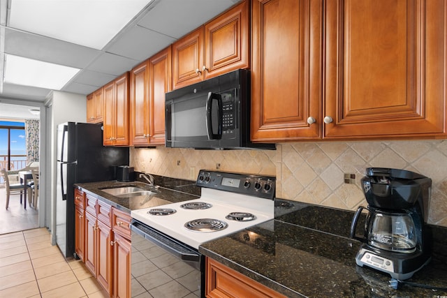 kitchen featuring a drop ceiling, dark stone counters, sink, black appliances, and light tile patterned floors