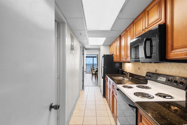 kitchen featuring a paneled ceiling, sink, black appliances, light tile patterned floors, and dark stone countertops