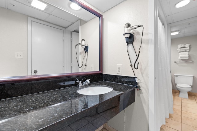 bathroom with tile patterned floors, a drop ceiling, toilet, and sink