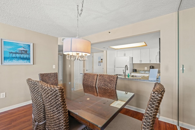 dining room with sink, dark wood-type flooring, a textured ceiling, and a notable chandelier