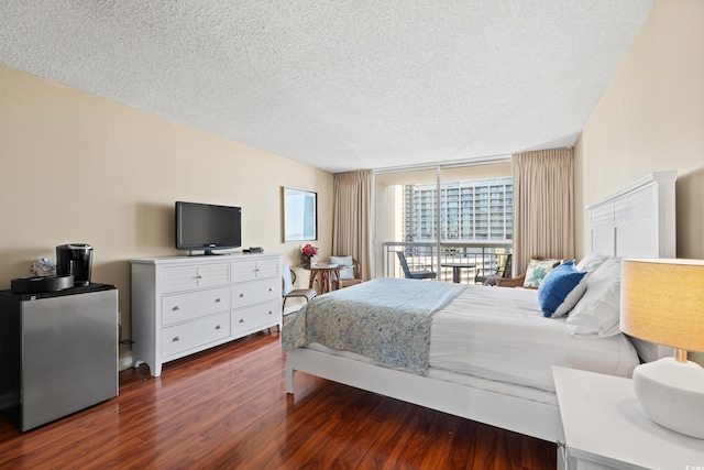 bedroom with a textured ceiling, a wall of windows, dark wood-type flooring, and stainless steel refrigerator