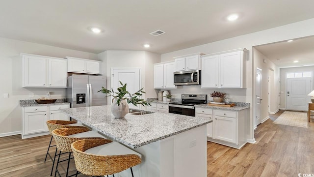 kitchen featuring a kitchen island with sink, white cabinetry, stainless steel appliances, and light hardwood / wood-style floors