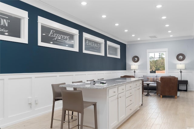 kitchen featuring white cabinets, a center island, light stone countertops, and ornamental molding