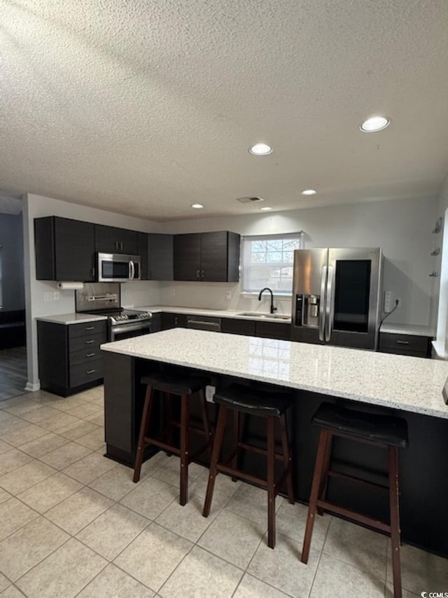 kitchen with a kitchen breakfast bar, appliances with stainless steel finishes, light stone counters, sink, and a center island