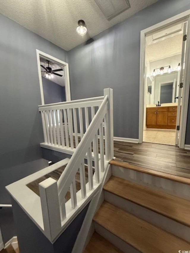 staircase featuring hardwood / wood-style flooring, ceiling fan, and a textured ceiling