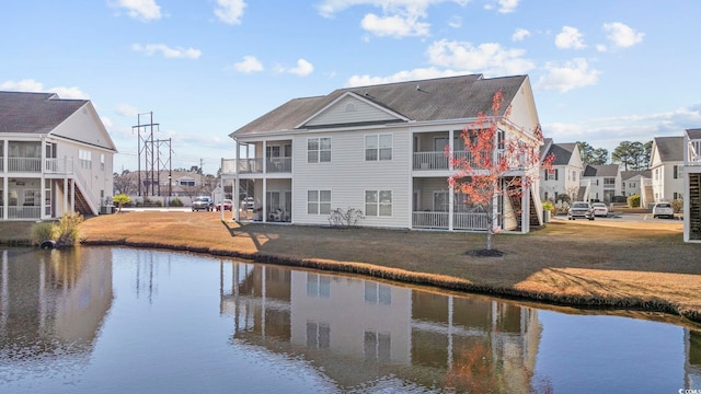 rear view of property with a yard, a balcony, and a water view