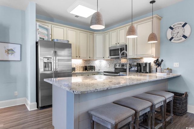 kitchen with cream cabinetry, kitchen peninsula, stainless steel appliances, and hanging light fixtures