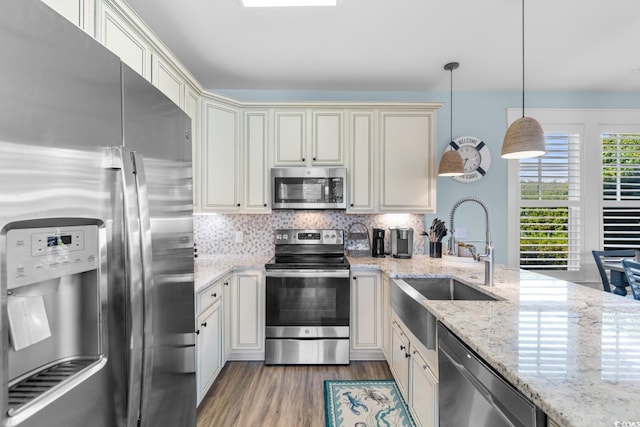 kitchen with light stone countertops, sink, hanging light fixtures, stainless steel appliances, and cream cabinets