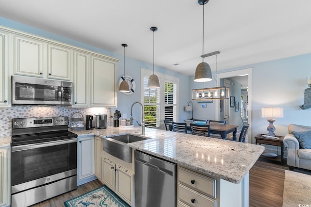 kitchen featuring kitchen peninsula, stainless steel appliances, sink, decorative light fixtures, and dark hardwood / wood-style floors