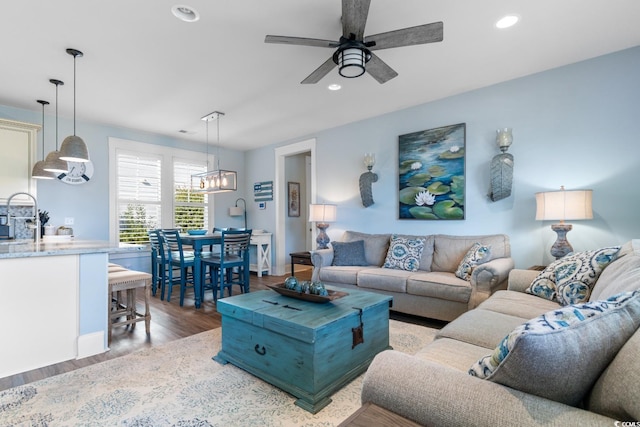 living room with hardwood / wood-style floors, ceiling fan with notable chandelier, and sink