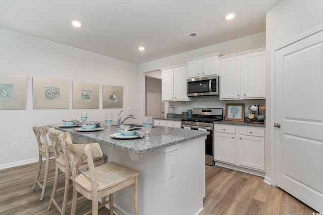 kitchen with white cabinets, a kitchen island with sink, stainless steel appliances, and a breakfast bar area