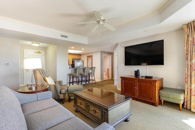 carpeted living room with ceiling fan, a raised ceiling, and ornamental molding