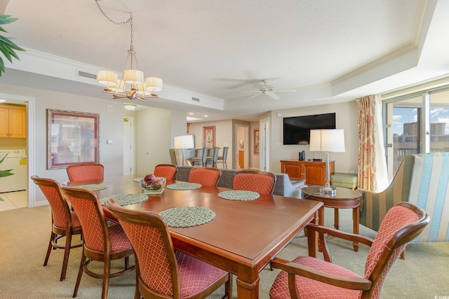 carpeted dining space featuring washer and dryer, ceiling fan with notable chandelier, a tray ceiling, and ornamental molding