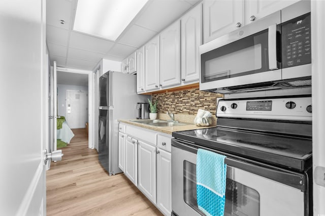 kitchen with appliances with stainless steel finishes, a paneled ceiling, tasteful backsplash, sink, and white cabinetry