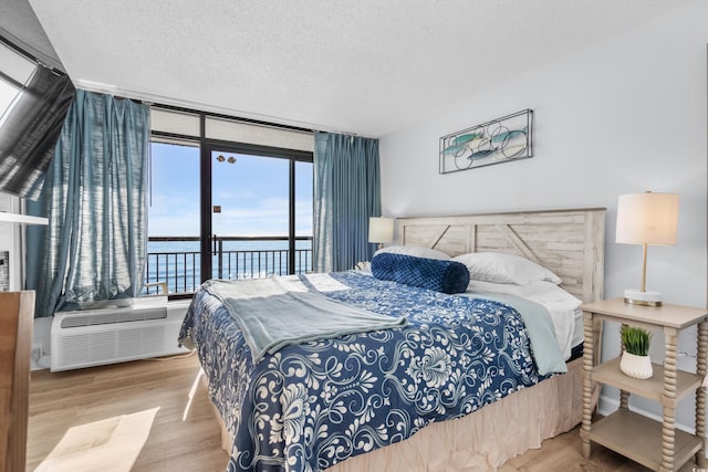 bedroom with floor to ceiling windows, a wall mounted AC, a textured ceiling, a water view, and hardwood / wood-style flooring