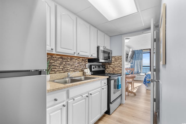 kitchen with appliances with stainless steel finishes, a paneled ceiling, backsplash, sink, and white cabinetry