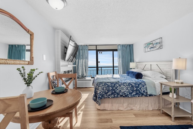 bedroom featuring expansive windows, access to exterior, light wood-type flooring, and a textured ceiling