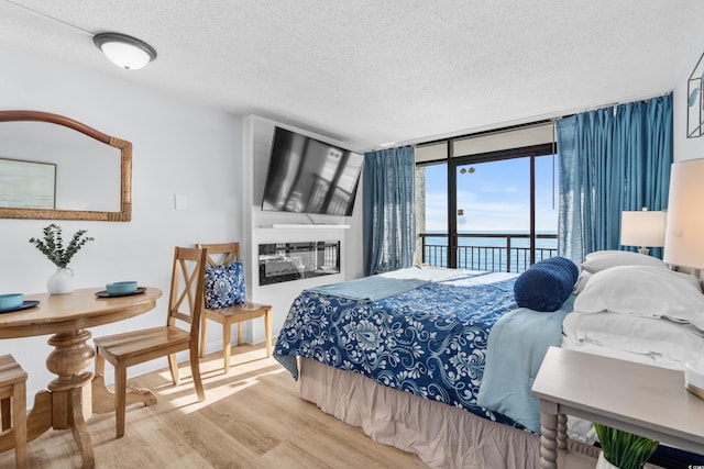 bedroom with hardwood / wood-style flooring, access to exterior, a wall of windows, and a textured ceiling