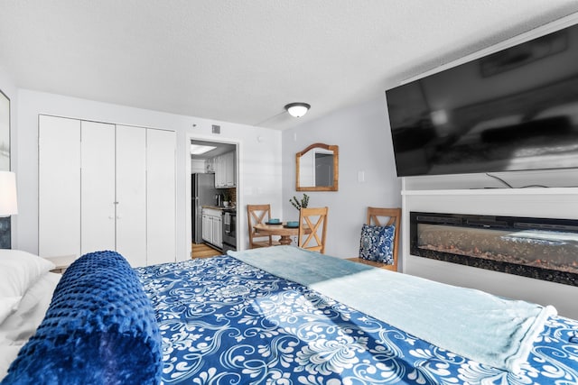 bedroom with a textured ceiling, stainless steel refrigerator, and a closet