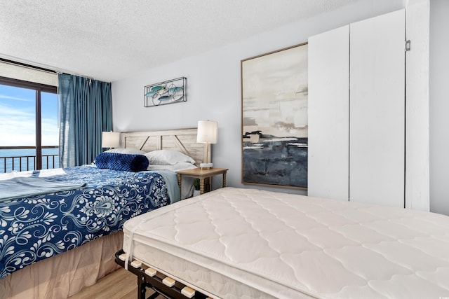 bedroom with hardwood / wood-style flooring, a water view, a textured ceiling, and access to outside