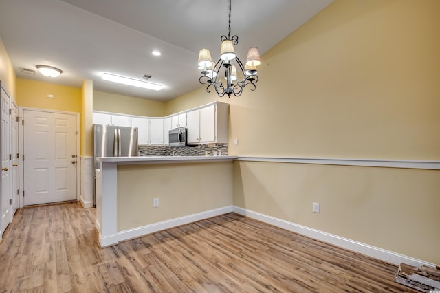 kitchen featuring white cabinets, light hardwood / wood-style flooring, appliances with stainless steel finishes, kitchen peninsula, and a chandelier