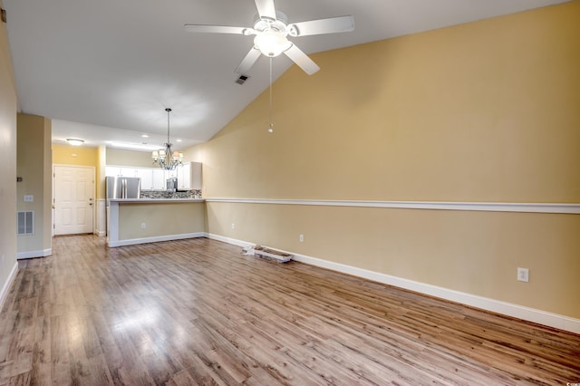 unfurnished living room featuring ceiling fan with notable chandelier, vaulted ceiling, and light wood-type flooring