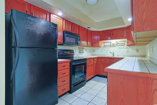 kitchen featuring black appliances, a raised ceiling, sink, light tile patterned floors, and tile counters