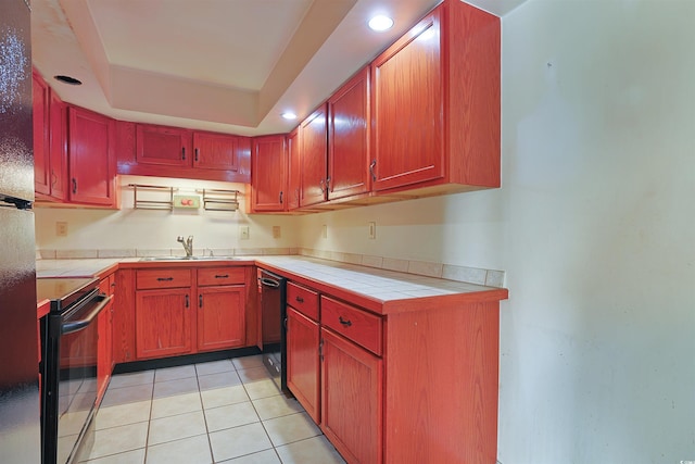 kitchen featuring black appliances, sink, light tile patterned floors, a tray ceiling, and tile counters