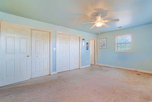 unfurnished bedroom featuring ceiling fan, light colored carpet, and multiple closets