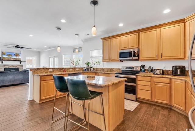 kitchen with dark hardwood / wood-style flooring, a breakfast bar, stainless steel appliances, ceiling fan, and a center island