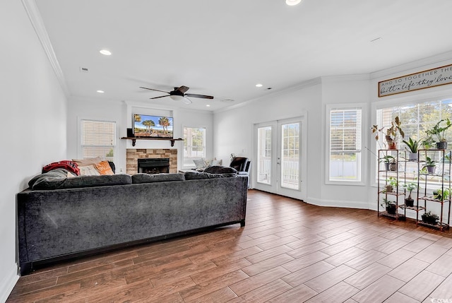 living room with a stone fireplace, a wealth of natural light, ornamental molding, and ceiling fan