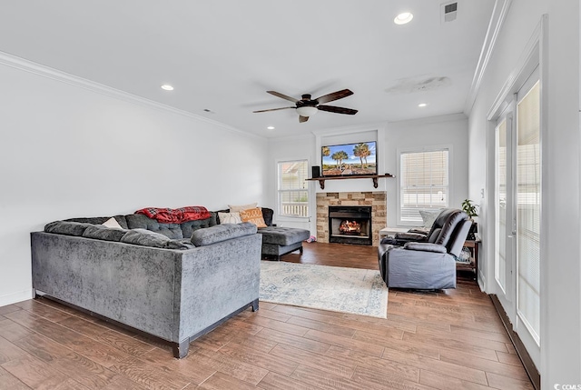 living room featuring a stone fireplace, ceiling fan, and crown molding