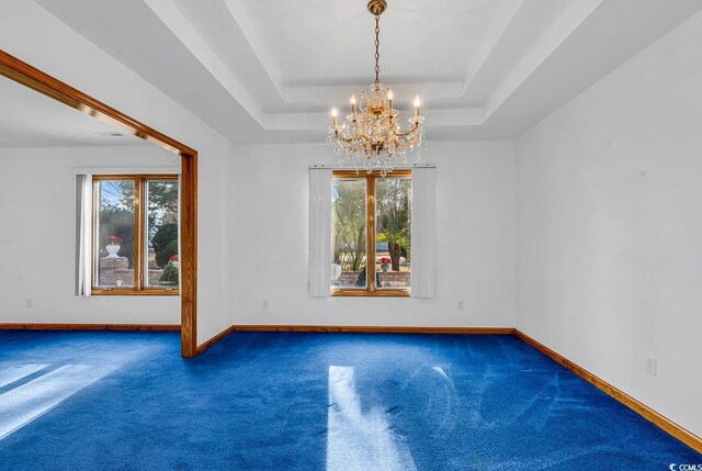 empty room with a chandelier, a raised ceiling, and dark carpet